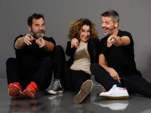 שני בחורים ובחורה יושבים על הרצפה מחייכים מצביעים לכיוון המצלמה
