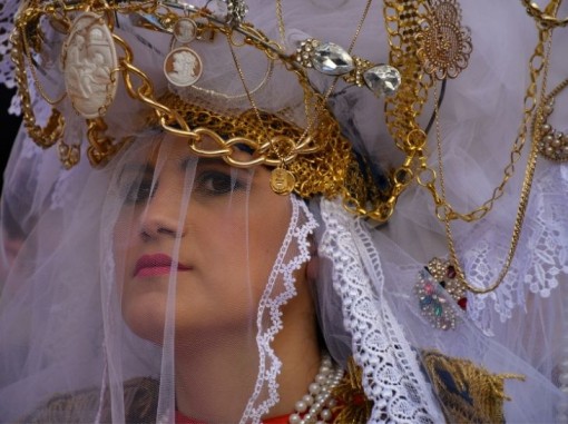 תקריב פני אישה סיציליאנית צעירה מקושטת במטפחת ראש לבנה ובתכשיטים